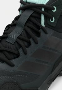 Μαύρο αθλητικό παπούτσι με υφή από διχτυωτό υλικό στο πάνω μέρος, πράσινες λεπτομέρειες, σκούρα κορδόνια και διακοσμητική πλευρική λωρίδα με τρεις ρίγες.