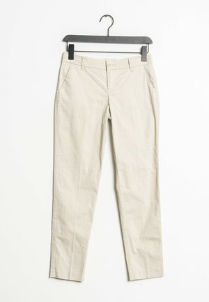 Beige slim-fit broek met voorzakken, riemlussen en een knoopsluiting, hangend aan een zwarte hanger tegen een witte achtergrond.