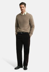 Béžový kašmírový svetr, pod ním smetanová košile s límečkem, doplněný tmavě burgundskými kordovýma kalhotama a černými koženými botami.