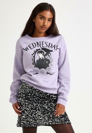 Sweatshirt lavande avec un motif d'une fille et le texte "Mercredi". Associé à une mini-jupe noire à paillettes.
