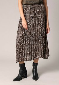 Jupe midi plissée à imprimé léopard dans des nuances de marron et noir, associée à des bottines noires à cheville. La jupe possède une taille élastique et une texture douce.