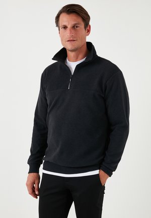 Black fleece pullover with a quarter zip, ribbed cuffs and hem, featuring a solid design with a smooth texture and casual fit.
