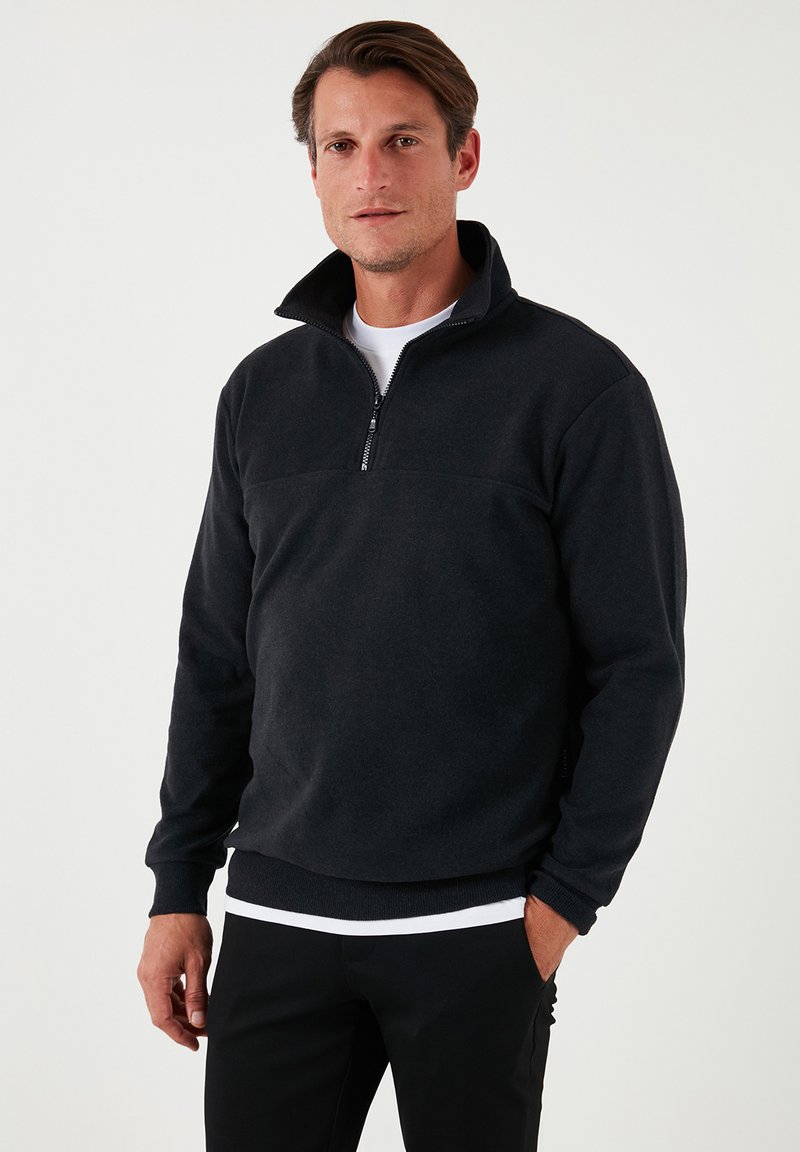 Pullover in pile nero con zipper a un quarto, polsi e orlo a coste, caratterizzato da un design semplice con una texture liscia e vestibilità informale.
