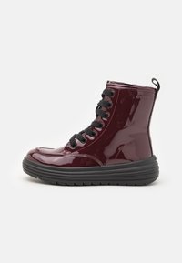 Burgundy patent leather ankle boots with black laces, a round toe, and a thick black rubber sole. Features a pull tab at the back.
