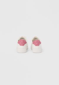 Λευκά αθλητικά παπούτσια με υφή στη ροζ φτέρνα, που διαθέτει επαναλαμβανόμενο λογότυπο, λείο υλικό και σχεδιασμό με χαμηλό πάνω μέρος.