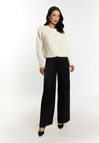 Ivoor gebreide cardigan met een textuurpatroon en parelaccenten, gecombineerd met zwarte wijde pantalon en zwarte puntige hakken.