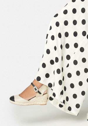 Mujer con alpargatas de cuña blancas con puntera negra y correa en el tobillo, combinadas con una falda blanca con grandes lunares negros.