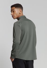 Groene langslavige shirt met een kraag, gladde textuur en knoopmanchetten. De achterkant heeft een ontspannen pasvorm en een ronde zoom.