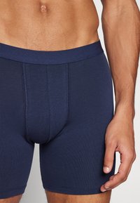Tengerészkék boxeralsó, rugalmas anyagból készült, testhezálló dizájnnal, elasztikus derékpánttal és lapos varrásokkal a kényelem és a támogatás érdekében.
