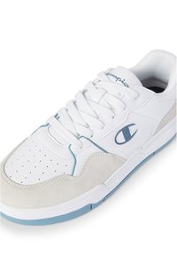 Weißer Sneaker aus Leder- und Wildledermaterialien, mit blauen Akzenten und einem perforierten Design im Zehenbereich. Champion-Logo an der Seite.