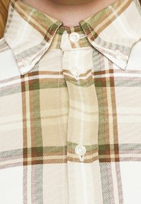 Koszula zapinana na guziki w beżowo-brązową kratę, z sztywnym kołnierzykiem, lekką teksturą materiału i guzikami perłowymi.