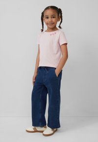Helles pinkes Baumwoll-T-Shirt mit drei roten Herzdetails am Halsausschnitt, kombiniert mit lässigen blauen Jeanshosen und weißen Turnschuhen.
