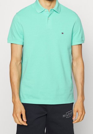 Polo tričko v mátové barvě, bavlněný materiál, krátké rukávy, dvouknoflíkový límec, logo na levé hrudi. Nosené s námořnickými sportovními šortkami.