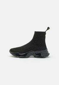 Baskets noires de style chaussette avec une tige en tricot texturé, ornées de petites clous ; elles sont dotées d'une semelle lustrée et contournée et d'une languette à l'arrière.