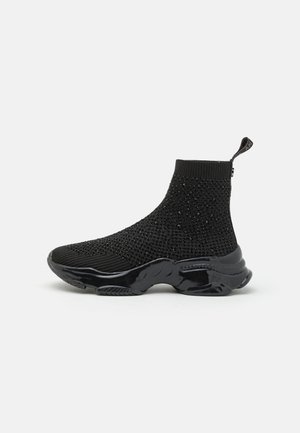 Schwarzer Sockensneaker mit einem strukturierten Strick-Obermaterial, verziert mit kleinen Nieten; verfügt über eine glänzende, konturierte Sohle und eine Zuglasche hinten.
