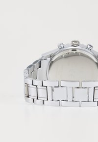 Montre en acier inoxydable argenté avec une finition polie, dotée d'un bracelet à maillons, d'un boîtier rond et d'une couronne texturée pour les réglages.