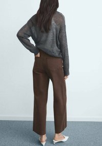 Pantalon marron à jambe large avec taille haute, associé à un pull en tricot gris ample, porté avec des mules blanches à talons. Texture lisse.