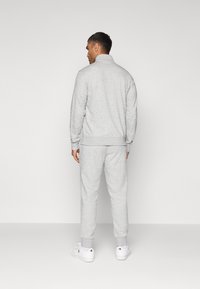 Grå hettegenser og joggebukse-sett, laget av myk stoff, med ribbet mansjetter og krage. Hvite sneakers kompletterer antrekket.