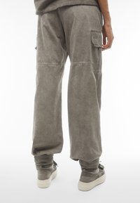 Pantaloni cargo morbidi in una tonalità grigia tenue, con tasche laterali, tessuto texturizzato e orli risvolti. Indossati con sneakers grigie.