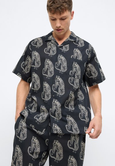 Kurzarmhemd aus schwarzem Stoff, das mit einem wiederholten Tigerdruck in Creme versehen ist. Das Hemd hat einen spitzen Kragen und eine Brusttasche.