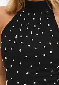 Top preto com pescoço halter, apresentando strass transparentes espalhados e detalhes em pérolas, textura lisa, design ajustado ao corpo e costuras mínimas.