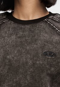 Μαύρο βαμβακερό φούτερ με υφασμάτινη υφή, διαθέτει ριμπ λαιμόκοψη και μικρό κεντητό λογότυπο στο στήθος.