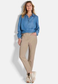 Lichtblauw denim overhemd met knoopsluiting, gecombineerd met beige op maat gemaakte broek en lichtgekleurde sneakers met een gestructureerd patroon.