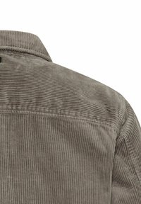 Close-up van het achterste schoudergedeelte van een taupe corduroy jas met verticale ribbels en zichtbare stikdetails.