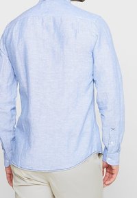 Chemise boutonnée à rayures bleu clair avec un col standard et des manches longues, dotée d'un ourlet arrondi et de poignets boutonnés.