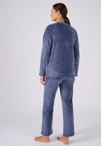 Conjunto de loungewear de forro polar azul que presenta una textura acolchada en la parte superior y pantalones lisos, diseñado con un corte relajado y mangas largas.