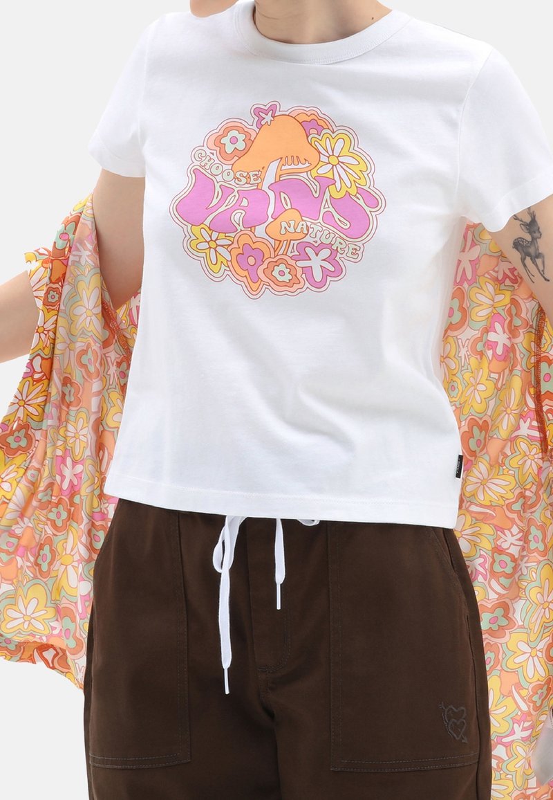 T-shirt blanc avec un motif rétro coloré floral et champignon avec l'inscription « Choose VANS Nature », porté avec un pantalon marron et une veste à motif floral.