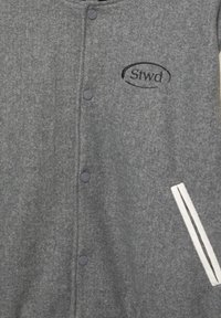 Šedá vlněná bunda s knoflíkovým zapínáním, vyšitým logem a kapsou s bílými pruhy na levé straně.