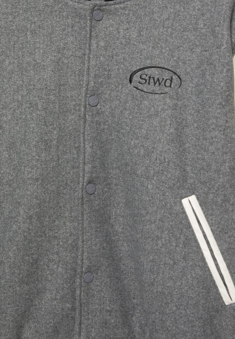 Veste en mélange de laine grise avec un devant  à boutons, logo brodé et une poche avec des rayures blanches sur le côté gauche.