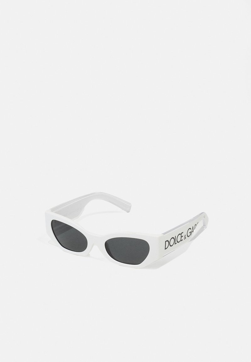 Lunettes de soleil blanches au design élégant et angulaire, avec des verres foncés et un logo sur le côté. Matériau plastique lisse avec une finition brillante.