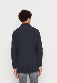 Mörkblå, långärmad jacka med rak passform och klassisk krage. Slät tyg med en rygghalkdetalj. Inga synliga detaljer eller mönster.