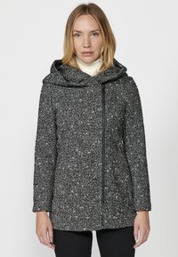 Čierno-biely škvrnitý kabát s veľkou kapucňou, zipsovým zapínaním, prispôsobeným strihom a dlhými rukávmi. Mäkky materiál, dĺžka do bokov.