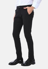 Pantaloni neri su misura con vestibilità slim, dotati di tasche laterali e chiusura con bottone. Realizzati in tessuto testurizzato, abbinati a mocassini neri lucidi.