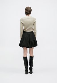 Μπεζ εφαρμοστό ριμπ πλεκτό πουλόβερ, μαύρη φουστάνι μπαλόνι, μαύρα γυαλιστερά μπότες μέχρι το γόνατο, λεία υφή, απλός σχεδιασμός, ορατές λεπτομέρειες ραφής.