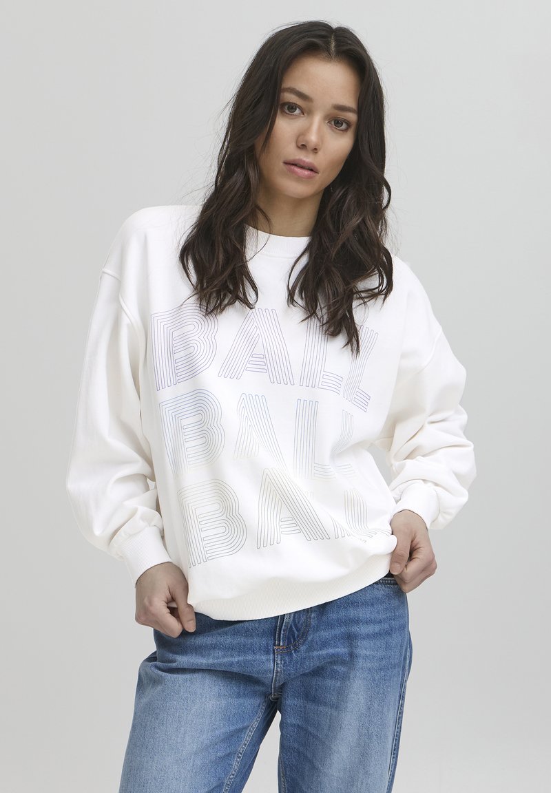 Sudadera blanca con la palabra "BALÓN" en texto rayado, corte holgado, con puños y dobladillo de canalé, combinada con jeans de mezclilla azul claro. Fondo neutro.