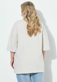 Lysebeige oversized t-shirt med korte ærmer, glat tekstur og en afslappet pasform, kombineret med lyseblå denimjeans.