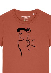 Rostorange Baumwoll-T-Shirt mit einer schwarzen Linienzeichnung eines Profils, das ein Design mit einem Halbmond und einer Sonne zeigt. Runder Halsausschnitt, kurze Ärmel.