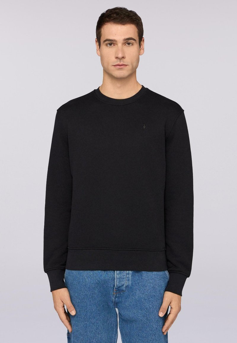 Svart sweatshirt med rund halsringning, ribbade ärmslut och nederkant. Har en liten logotyp på bröstet. Tyget verkar slätt och något strukturerat.