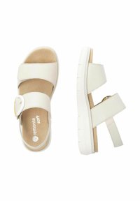 Sandales blanches avec deux sangles ajustables et une boucle ronde, présentant une semelle intérieure beige douce et une semelle en caoutchouc blanc texturé.