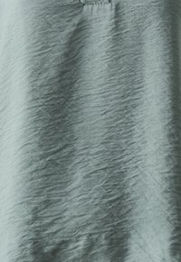 Light teal garment with a textured surface, featuring soft, wrinkled fabric and a discreet pocket detail at the neckline.