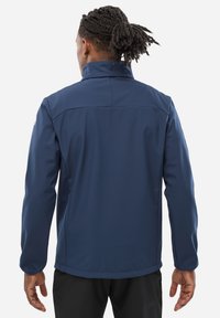 Navy softshell jacket with a high collar, long sleeves, and a smooth texture; features a fitted design and back seams for added detail.
