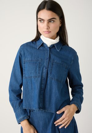Jeanshemd in tiefblau, mit kragen, durchgehendem Knopfverschluss und zwei Brusttaschen. Glatte Textur mit langen Ärmeln.