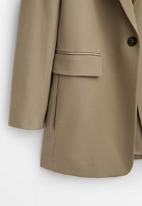 Beiger Blazer mit strukturiertem Design, ausgestattet mit Reverskragen, einem Knopfverschluss und einer Vordertasche. Textil mit einer strukturierten Oberfläche und glatter Haptik.