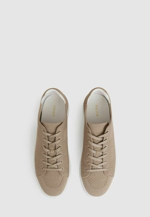 Baskets en tricot beige avec un dessus texturé, semelle blanche et six paires d'œillets pour les lacets. Design minimaliste, finition lisse, sans marque visible.