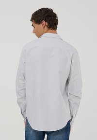 Camicia a maniche lunghe a righe in cotone bianco e azzurro chiaro. Presenta un colletto, polsini con bottoni sul retro e orlo curvo. Vestibilità classica.