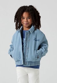 Helehall sinine teksajakk lõdva lõikega, millel on klõpsuga eesmine sulgemine, küljetaskud ja rinnal tikitud "Levi's".